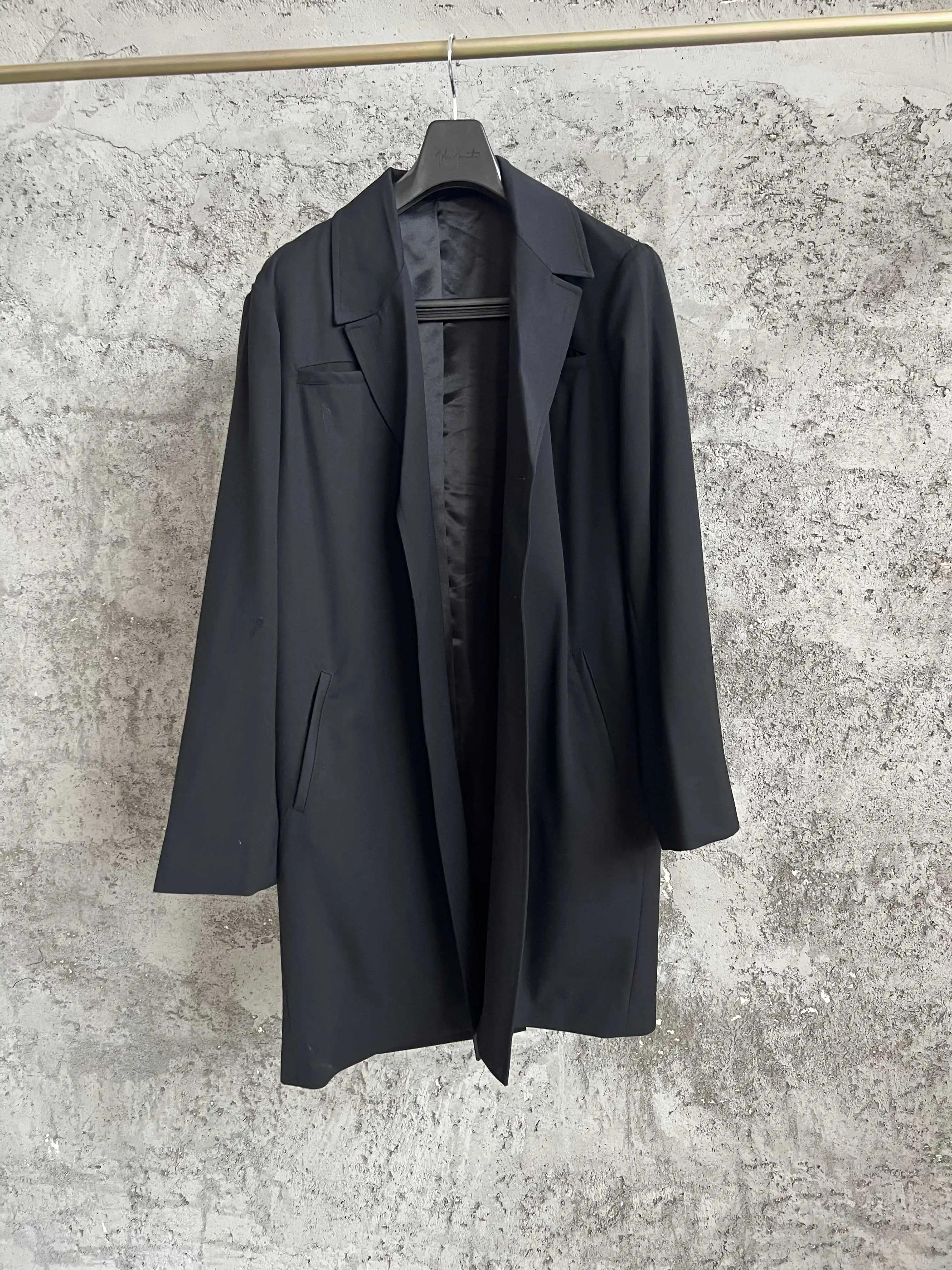 Un costume noir avec un revers incliné, un design à simple boutonnage et un ourlet irrégulier